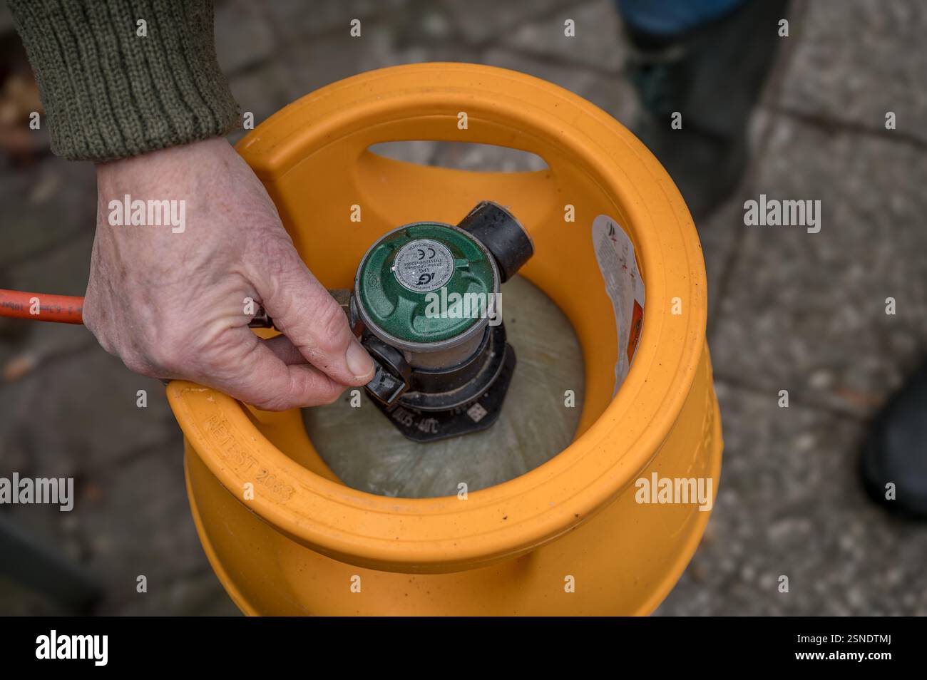 Bombola di gas gialla collegata con un tubo rosso e una mano che chiude il gas, Danimarca, 13 febbraio 2025 Foto Stock