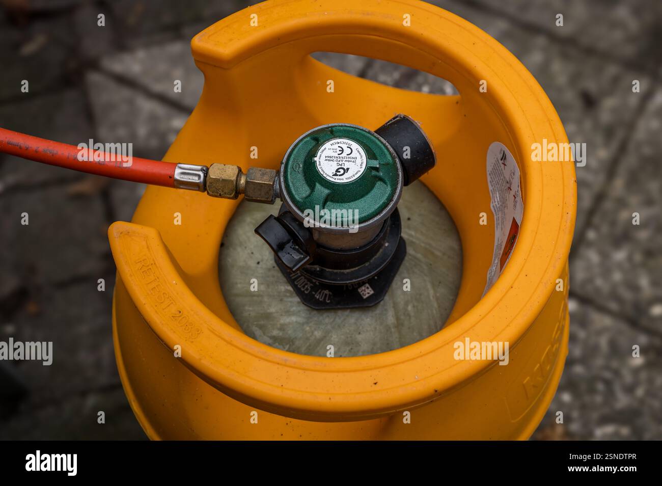 Bombola di gas gialla collegata con un tubo rosso e una mano che chiude il gas, Danimarca, 13 febbraio 2025 Foto Stock