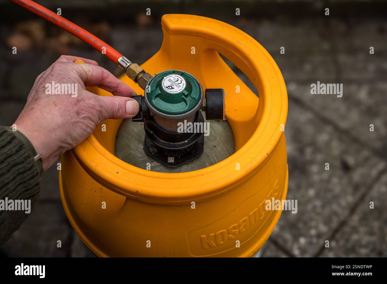 Bombola di gas gialla collegata con un tubo rosso e una mano che chiude il gas, Danimarca, 13 febbraio 2025 Foto Stock