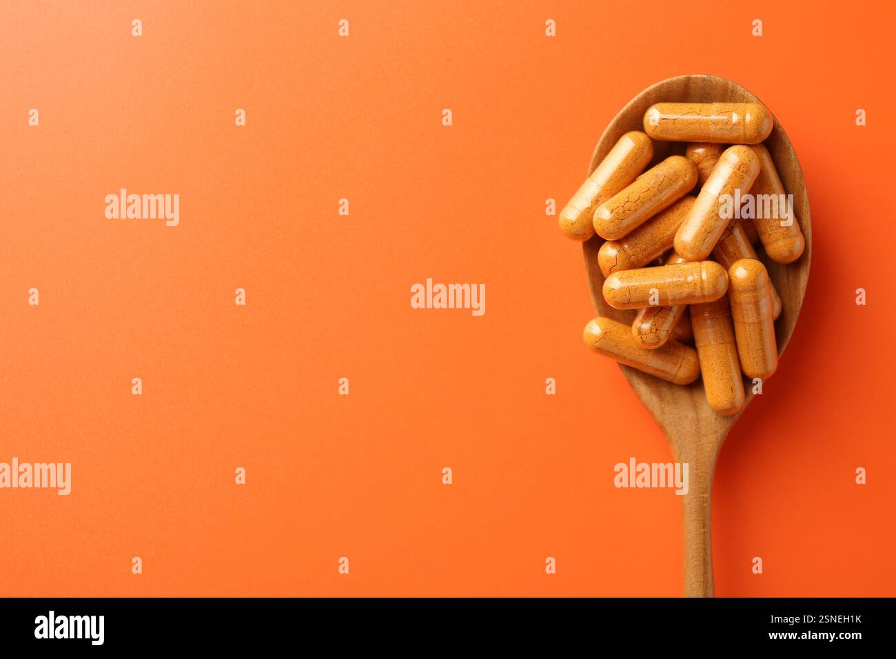 Capsule di curcuma in cucchiaio di legno su sfondo arancione, vista dall'alto Foto Stock