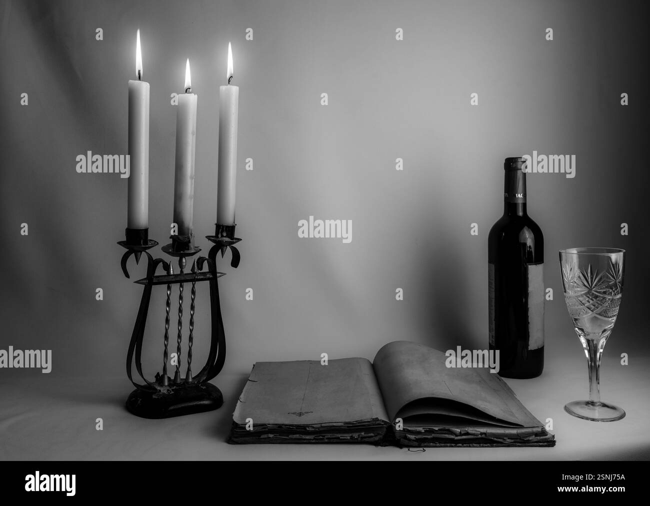 Una composizione STILL Life in bianco e nero con un libro vintage aperto, un antico candelabro con candele accese, una bottiglia di vino e un bicchiere, crea Foto Stock