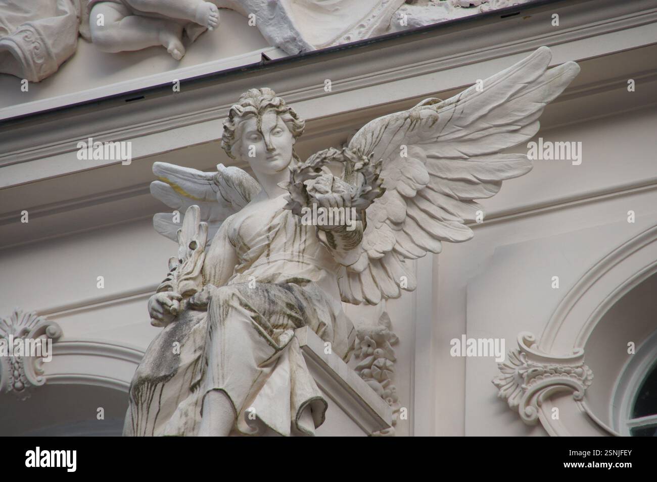 Una statua di angelo di pietra con ali allungate appollaiata su una sporgenza di un edificio moderno in Germania, Monaco. Il tutore architettonico è un simbolo del luppolo Foto Stock
