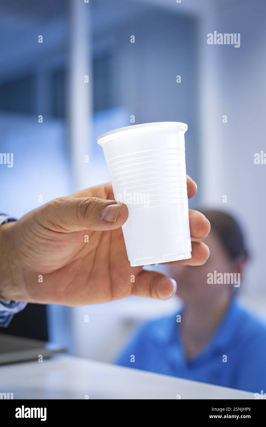 Una mano che tiene una tazza di plastica al banco della reception con sfondo sfocato, Urologia, Germania, Europa Foto Stock