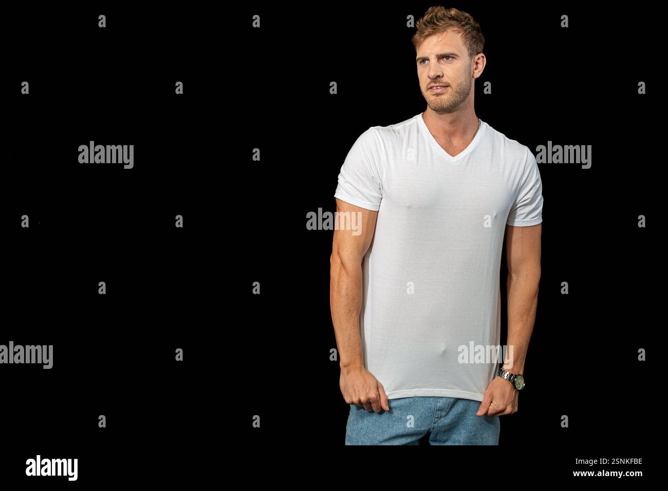 Un uomo biondo elegante indossa con sicurezza una classica t-shirt bianca e jeans blu, incarnando la moda disinvolta e lo stile casual moderno Foto Stock