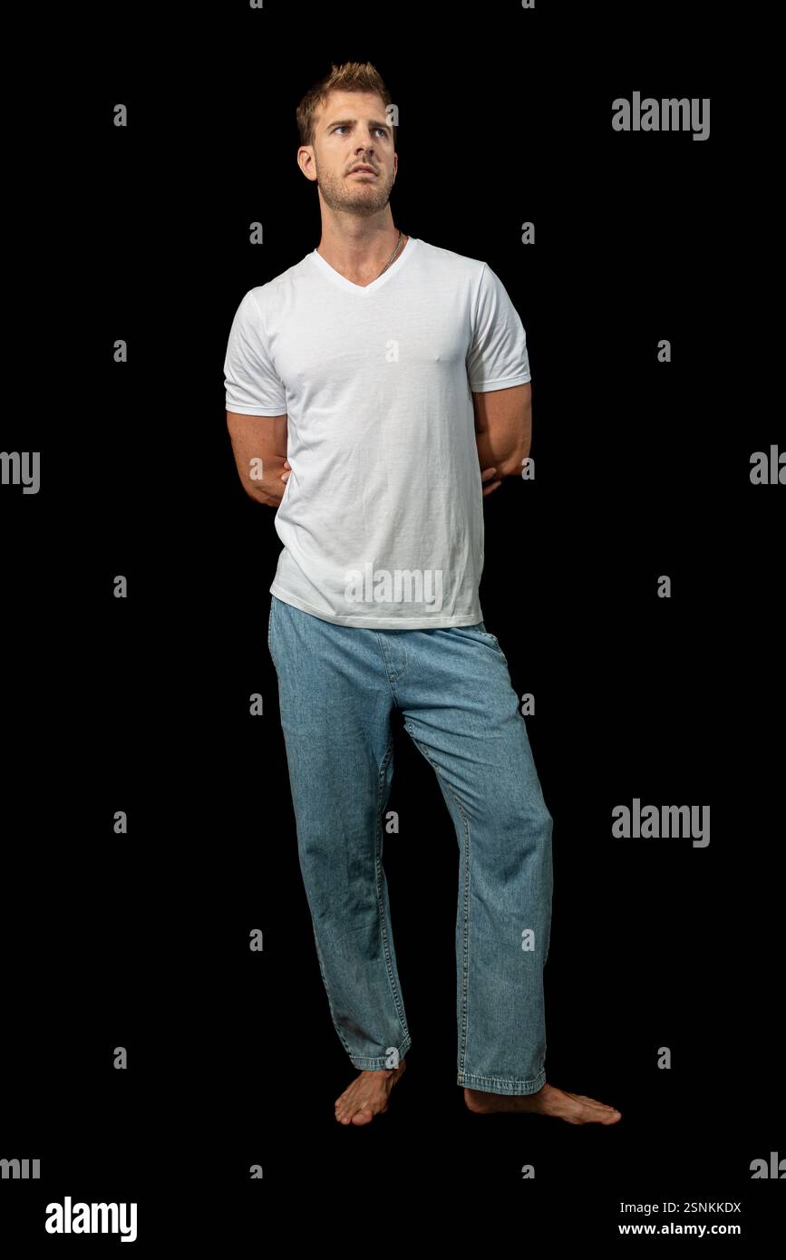 Un uomo biondo elegante indossa con sicurezza una classica t-shirt bianca e jeans blu, incarnando la moda disinvolta e lo stile casual moderno Foto Stock