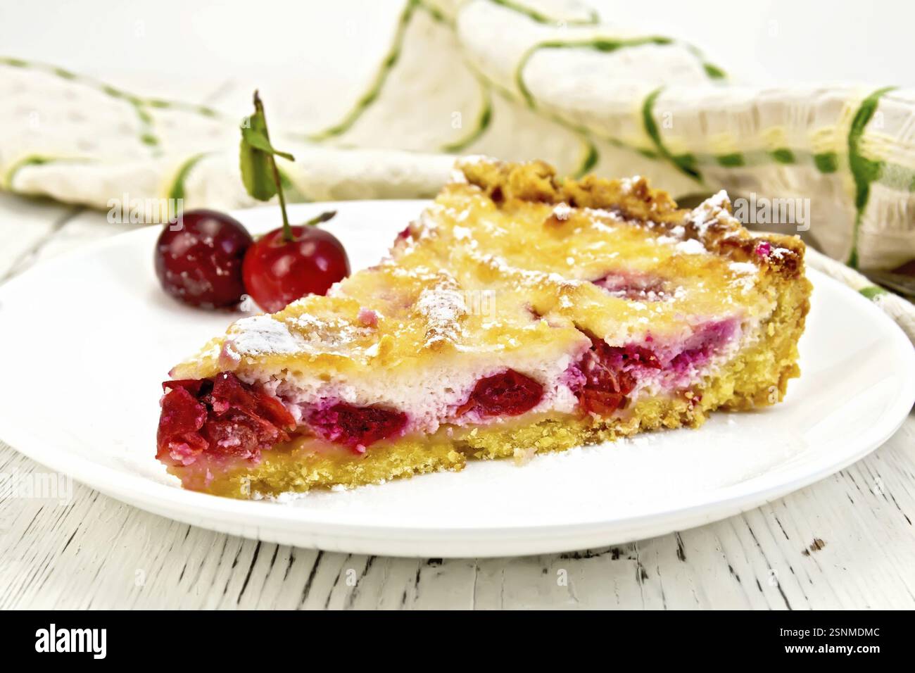 Torta con ciliegie e panna acida in un piatto, asciugamani su uno sfondo di tavole di legno Foto Stock
