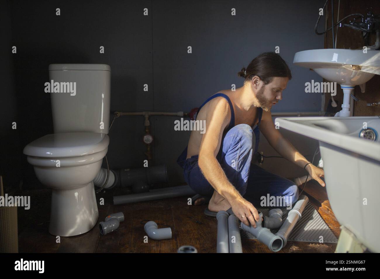 Idraulico che sistemava tubi sul pavimento del bagno con luce solare che scorre, accanto a un gabinetto Foto Stock