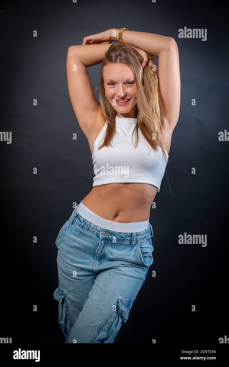 Una bella donna bionda indossa con sicurezza un look casual ma elegante, indossando una camicia bianca senza maniche e classici jeans blu Foto Stock