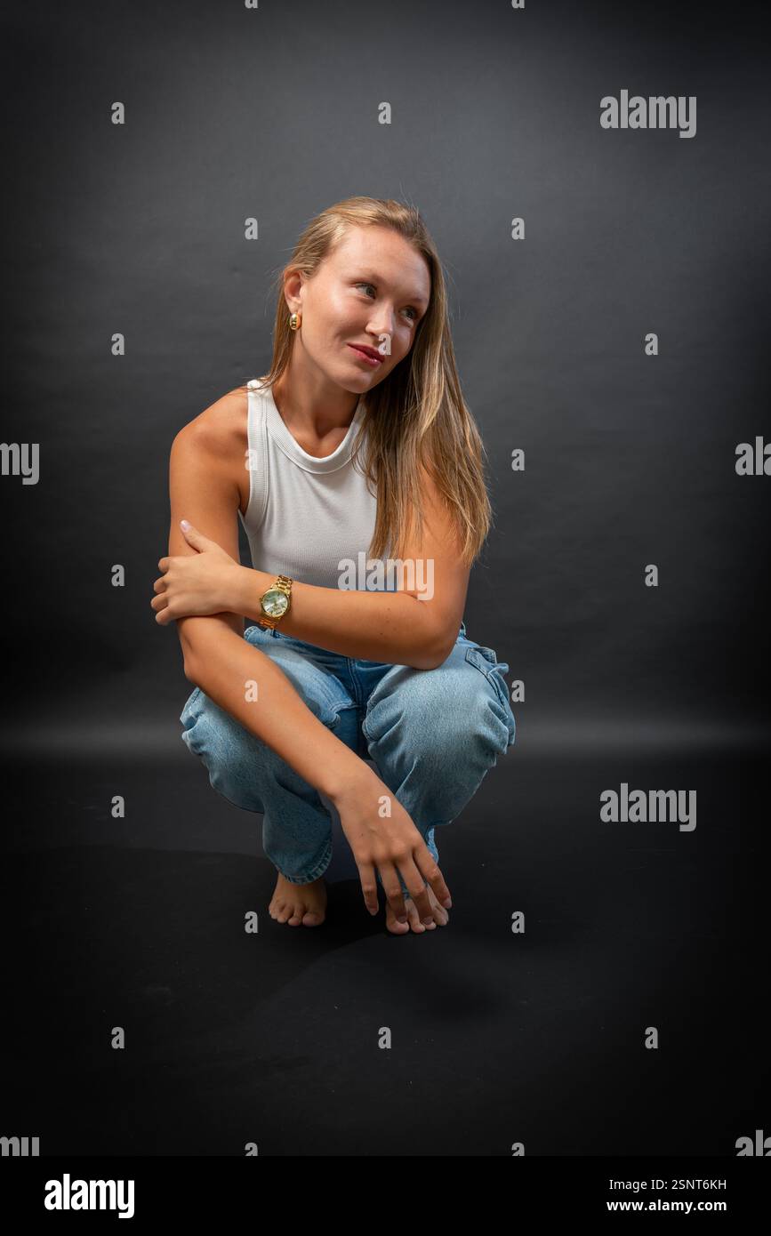 Una bella donna bionda indossa con sicurezza un look casual ma elegante, indossando una camicia bianca senza maniche e classici jeans blu Foto Stock