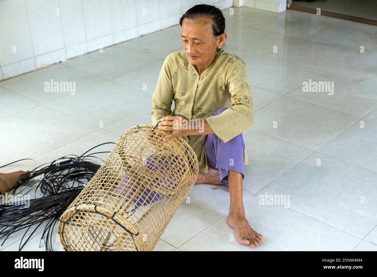 Una donna siede sul pavimento di un laboratorio rurale che produce trappole per pesci di bambù, Cho Lach, Vietnam, lunedì 11 novembre, 2024. Foto Stock