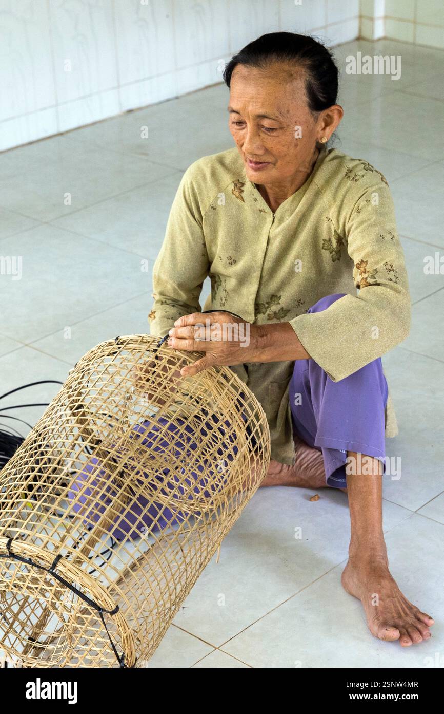 Una donna siede sul pavimento di un laboratorio rurale che produce trappole per pesci di bambù, Cho Lach, Vietnam, lunedì 11 novembre, 2024. Foto Stock