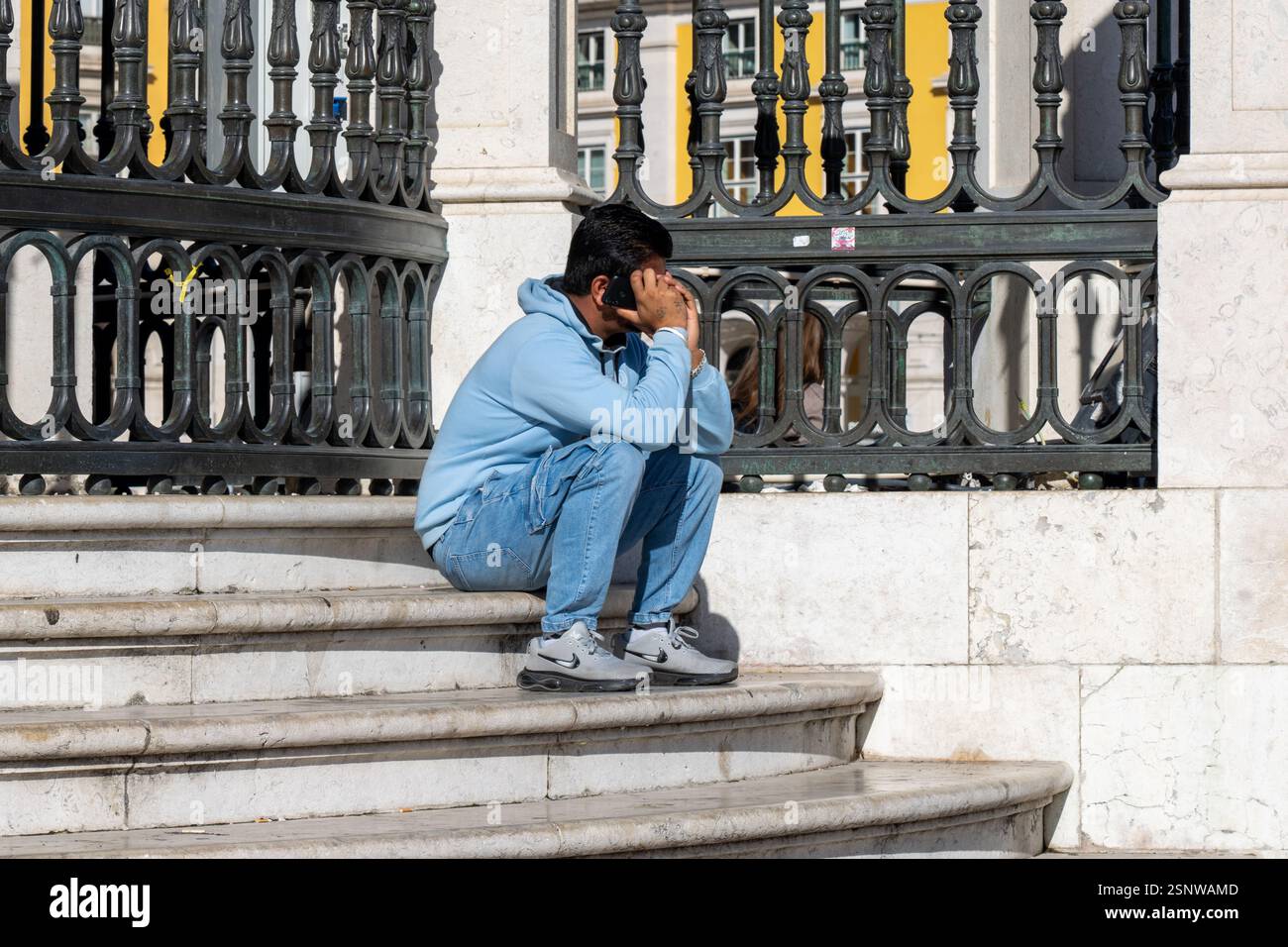 Lisbona Portogallo - settembre 28 2024: Uomo seduto su gradini fuori a parlare su un cellulare a Lisbona in Portogallo Foto Stock