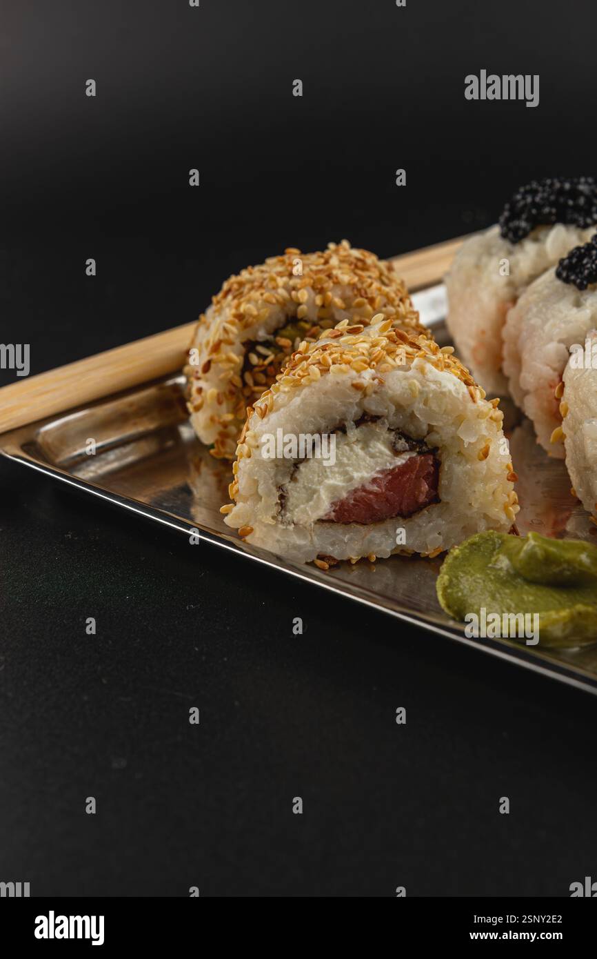 Deliziosi sushi roll sono disposti su un piatto metallico, con una varietà di ripieni. I panini sono guarniti con semi di sesamo e accompagnati Foto Stock