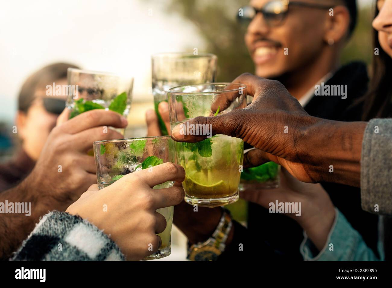 Primo piano di occhiali mojito a più mani in un ambiente all'aperto festoso. Un momento di festa e amicizia. Foto Stock