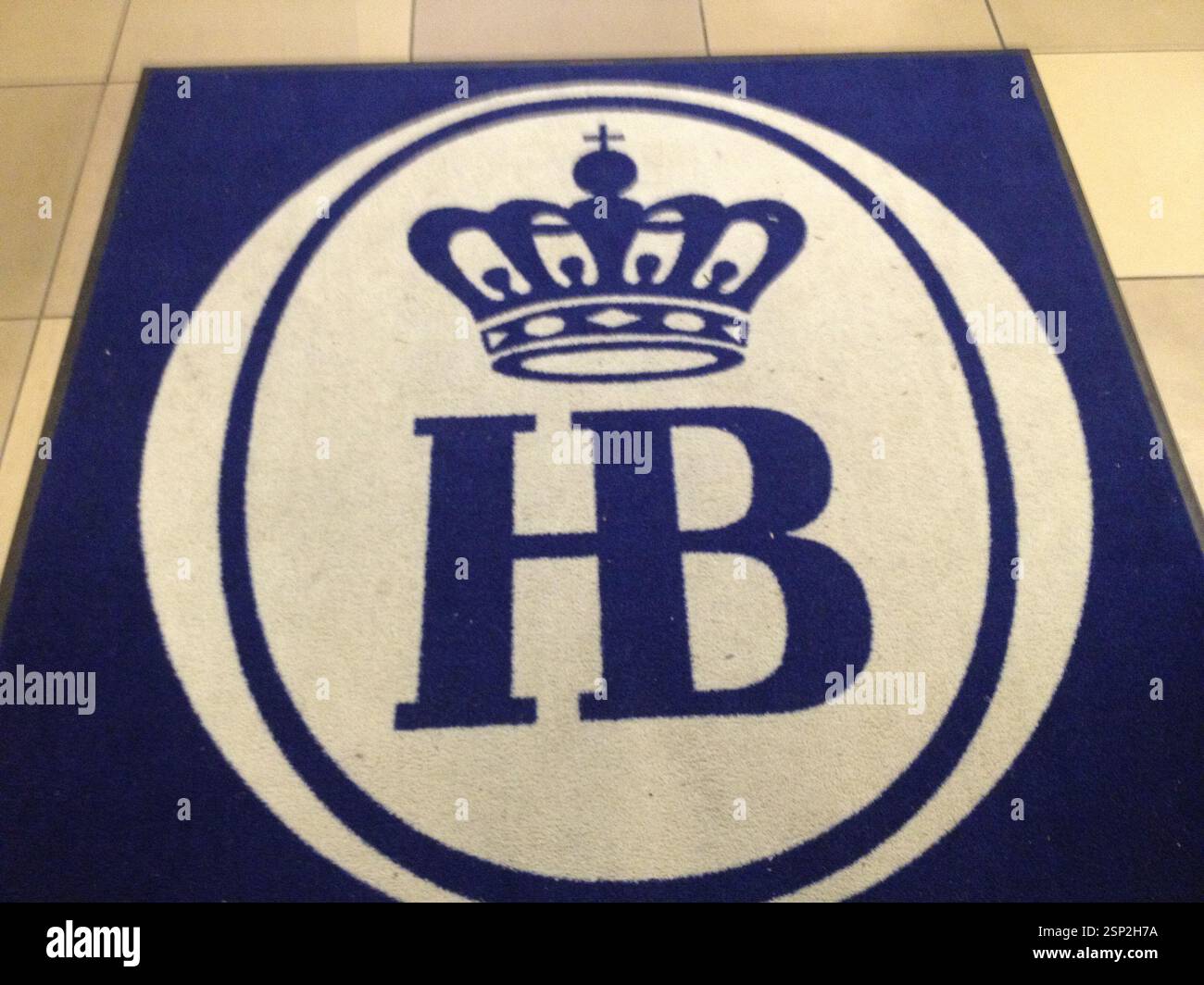 Tappetino blu con ovale bianco contenente la corona blu sopra le iniziali HB. Logo per il birrificio Hofbräuhaus, Germania, Monaco di Baviera. Probabile tappetino d'ingresso per il ristorante o. Foto Stock
