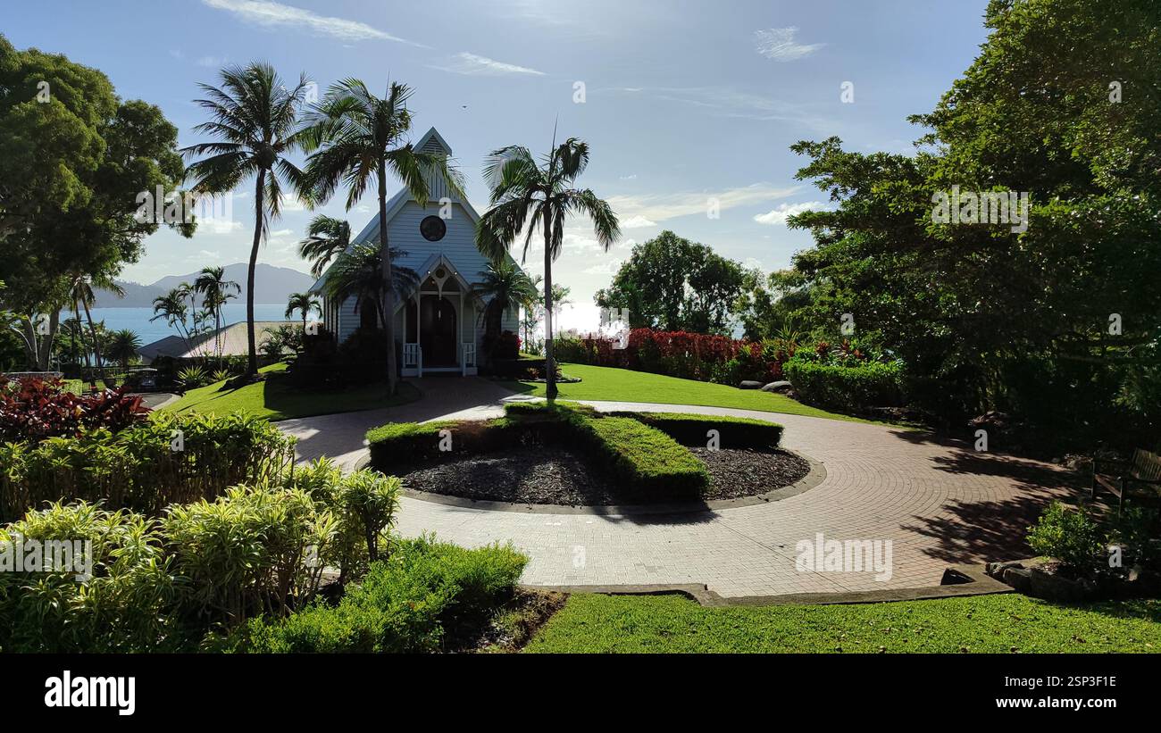 Paradiso di Hamilton Island: Una chiesa bianca con un tetto rosso corona una collina, palme che ondeggiano accanto ad essa. L'oceano turchese si estende sotto, creatina Foto Stock