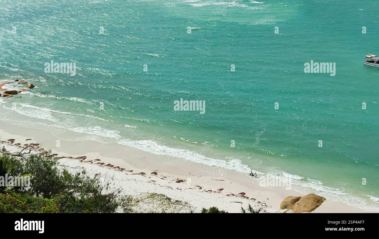 Una spiaggia sabbiosa con dolci onde che lambiscono la riva e una piccola barca che galleggia pacificamente in lontananza. E' una scena tranquilla, perfetta per una tranquilla Foto Stock