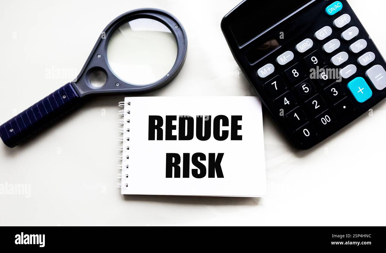 Sul notebook è presente un'iscrizione per ridurre i rischi, accanto ad essa è presente una calcolatrice e una lente di ingrandimento. Il concetto di urgenza e importanza Foto Stock