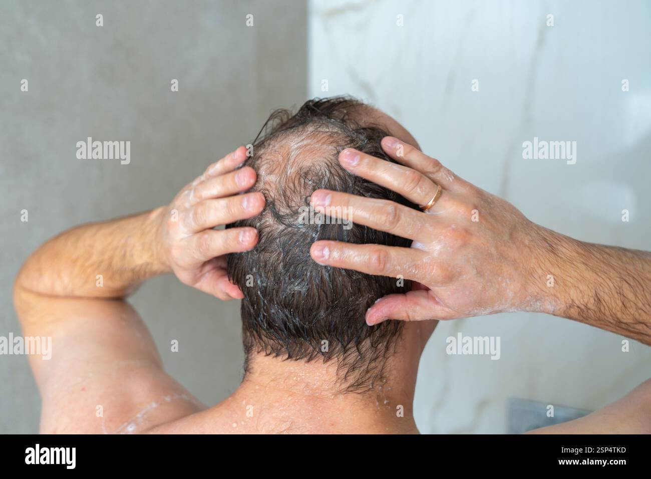 l'uomo sapone la testa nella doccia, la testa con un punto calvo, in piedi con la schiena verso la telecamera, primo piano. Riprese 4K di alta qualità Foto Stock