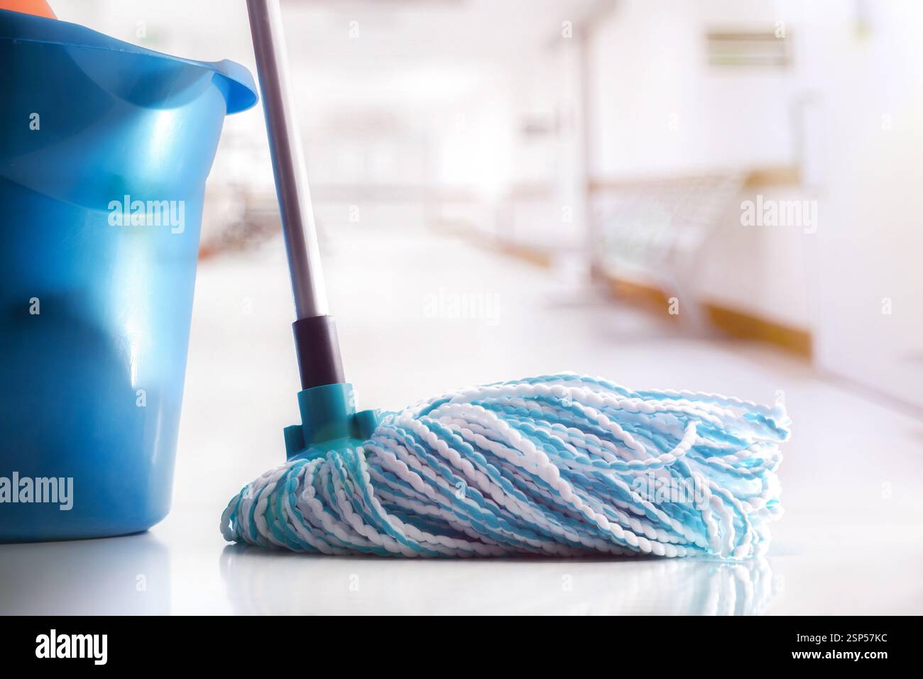 Spazzolone con fibre bianche e blu e secchio per spazzolone blu su un pavimento riflettente pulito in un corridoio bianco. Vista frontale. Foto Stock