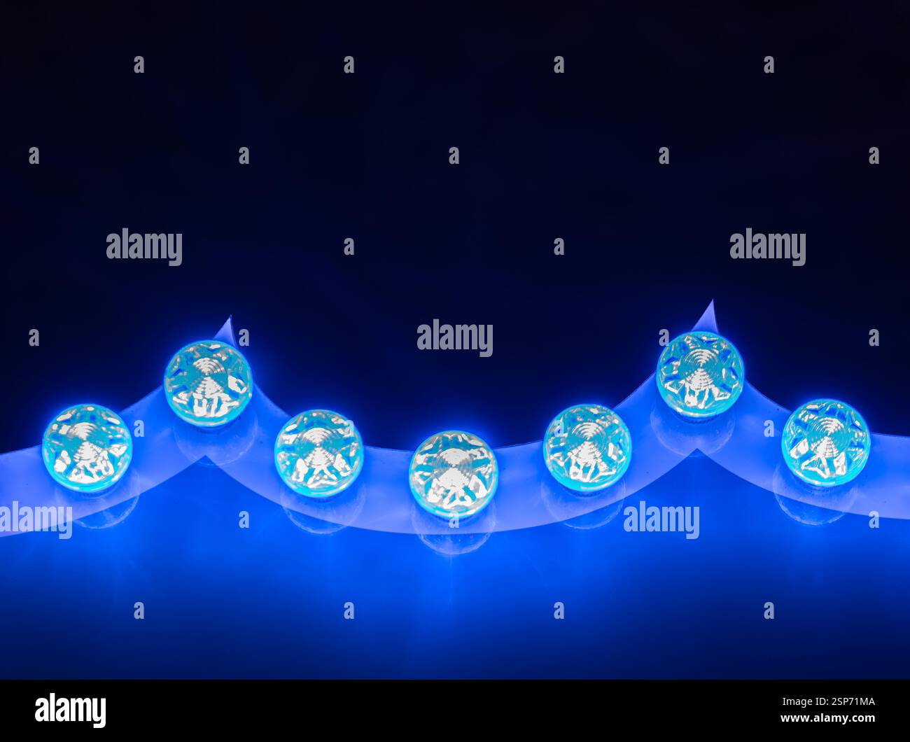 Una serie decorativa di luci LED blu brillanti a forma di ornamenti rotondi, su uno sfondo scuro. Le luci emettono un bagliore vibrante, creando un Foto Stock