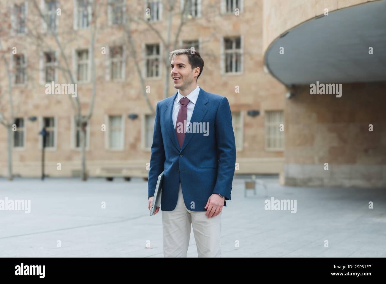 Uomo d'affari che cammina fuori dall'ufficio tenendo un portatile sorridente Foto Stock