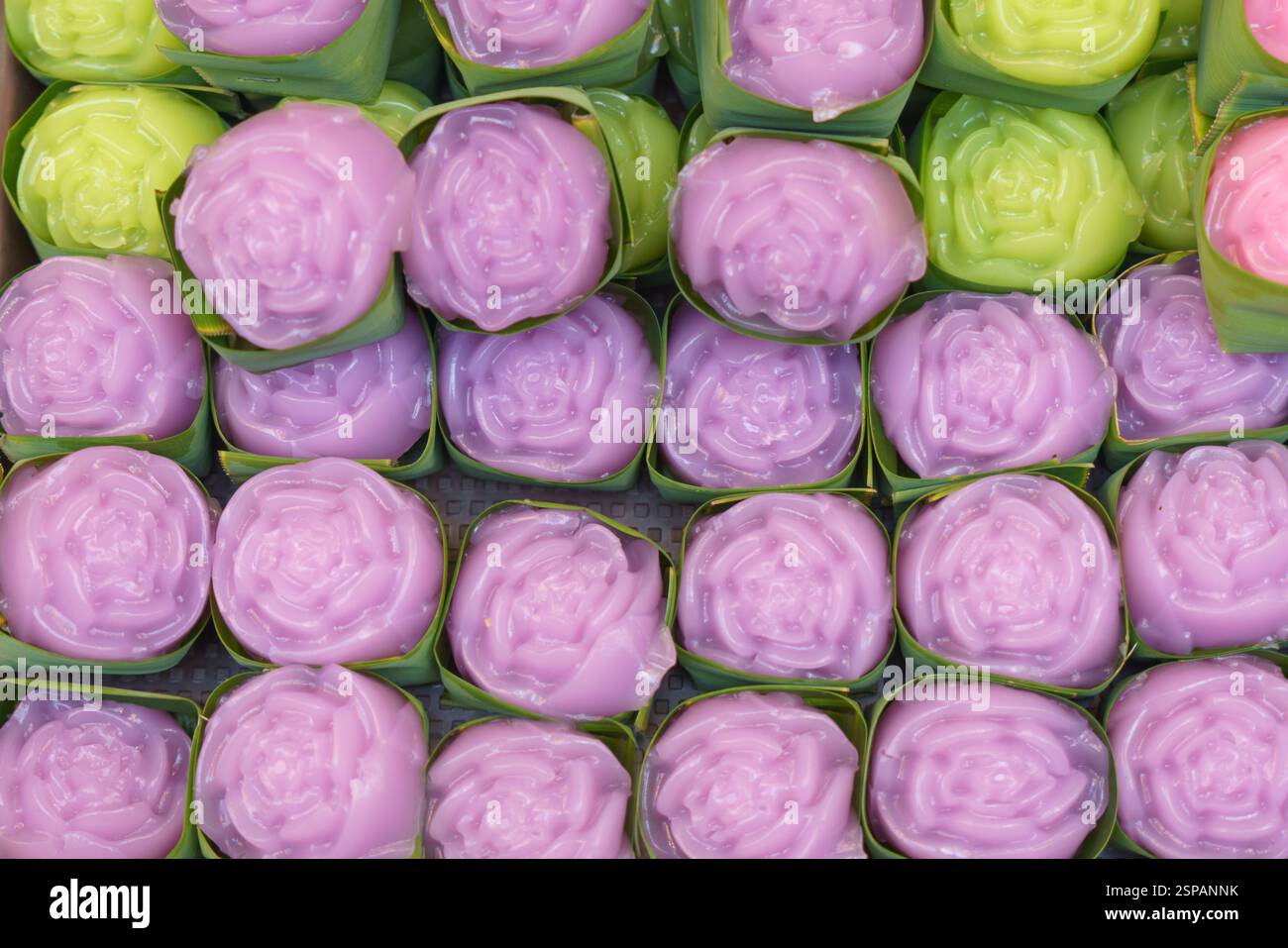 Primo piano di delicati dessert in gelatina tailandese a forma di rosa con morbide sfumature pastello (rosa, verde e viola) avvolti in piccole tazze di foglie di banana Foto Stock