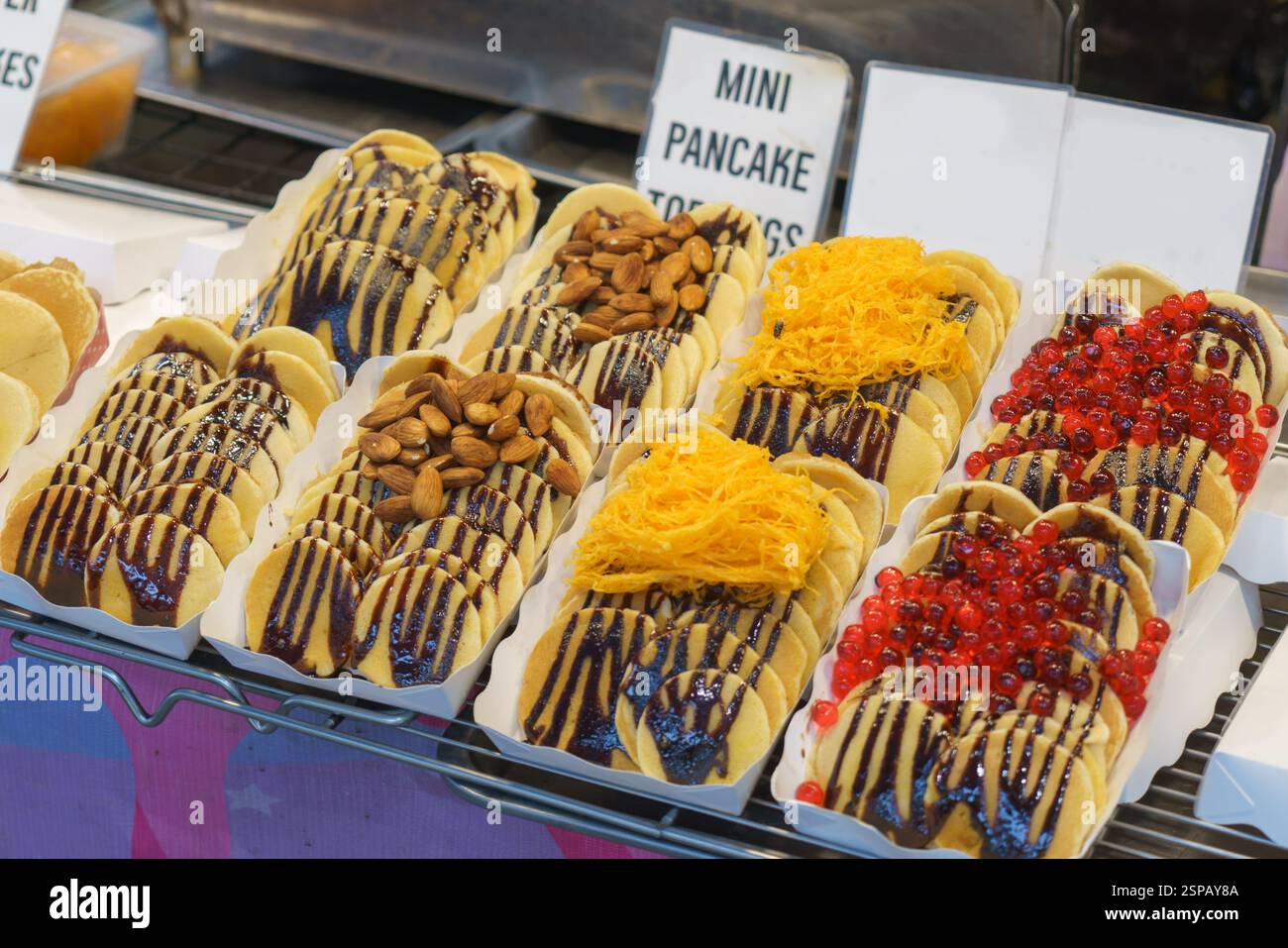 Primo piano di mini pancake conditi con salsa al cioccolato e decorati con vari condimenti, tra cui mandorle, filetti d'uovo dorati (fu Thong) e br Foto Stock