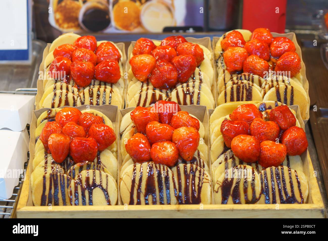 primo piano di mini frittelle appena preparate, ricoperte di fragole succose e condite con salsa al cioccolato. Questi dolcetti, esposti a un desse Foto Stock