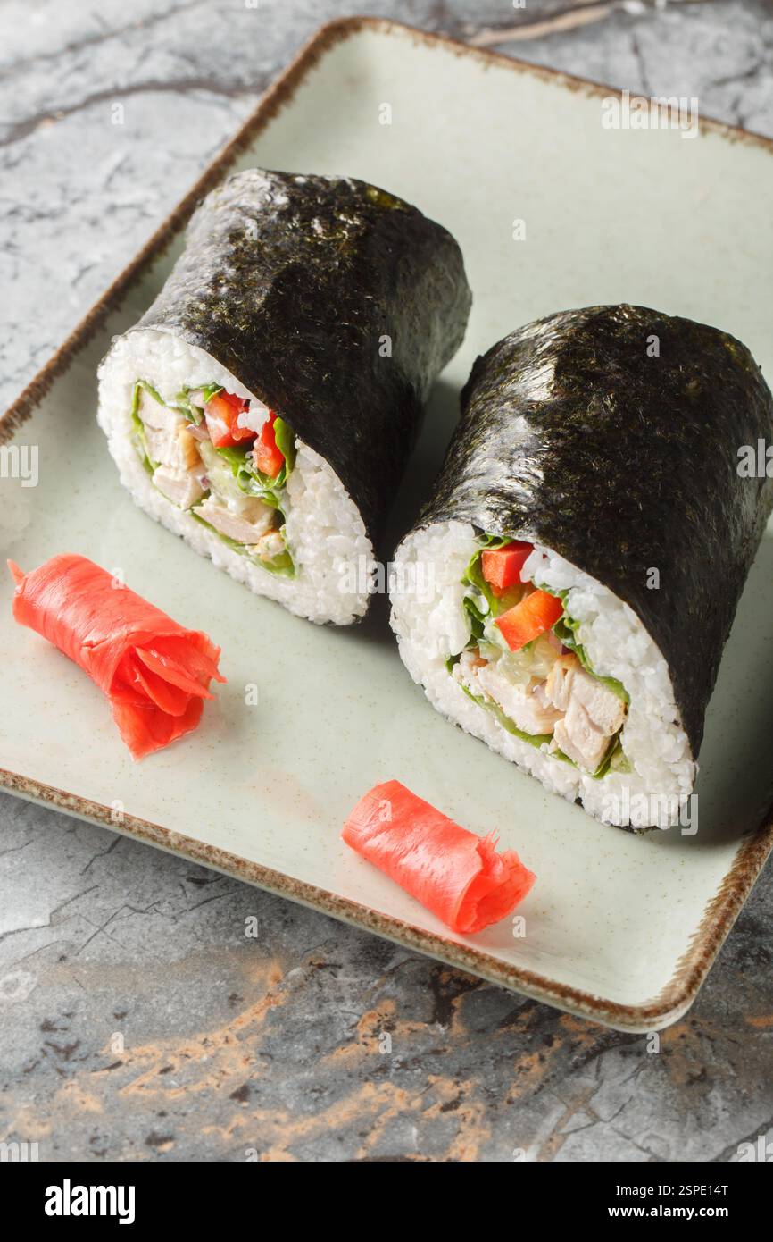 Burrito sushi fresco con riso, pollo, formaggio spalmabile, verdure e lattuga avvolti in alghe nori da vicino in un piatto sul tavolo. Verticale Foto Stock