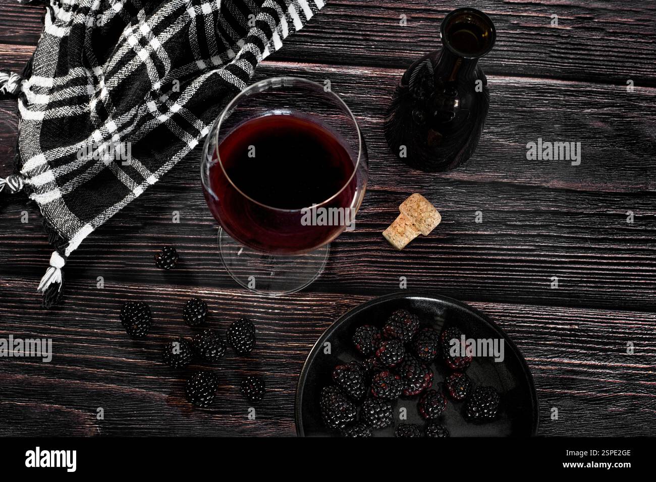 Vino rosso in un bicchiere accanto a una bottiglia nera e alcune more su un tavolo di legno in un'atmosfera rustica e scura, vista dall'alto Foto Stock
