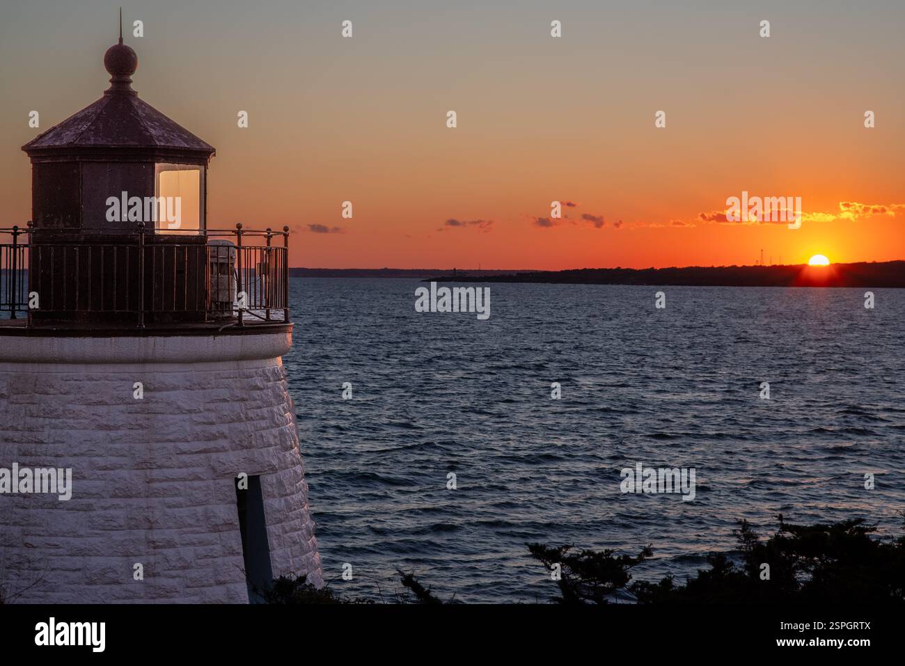 Un faro del Rhode Island al tramonto con il sole incandescente che proietta una luce dorata sulle onde dell'oceano. Foto Stock