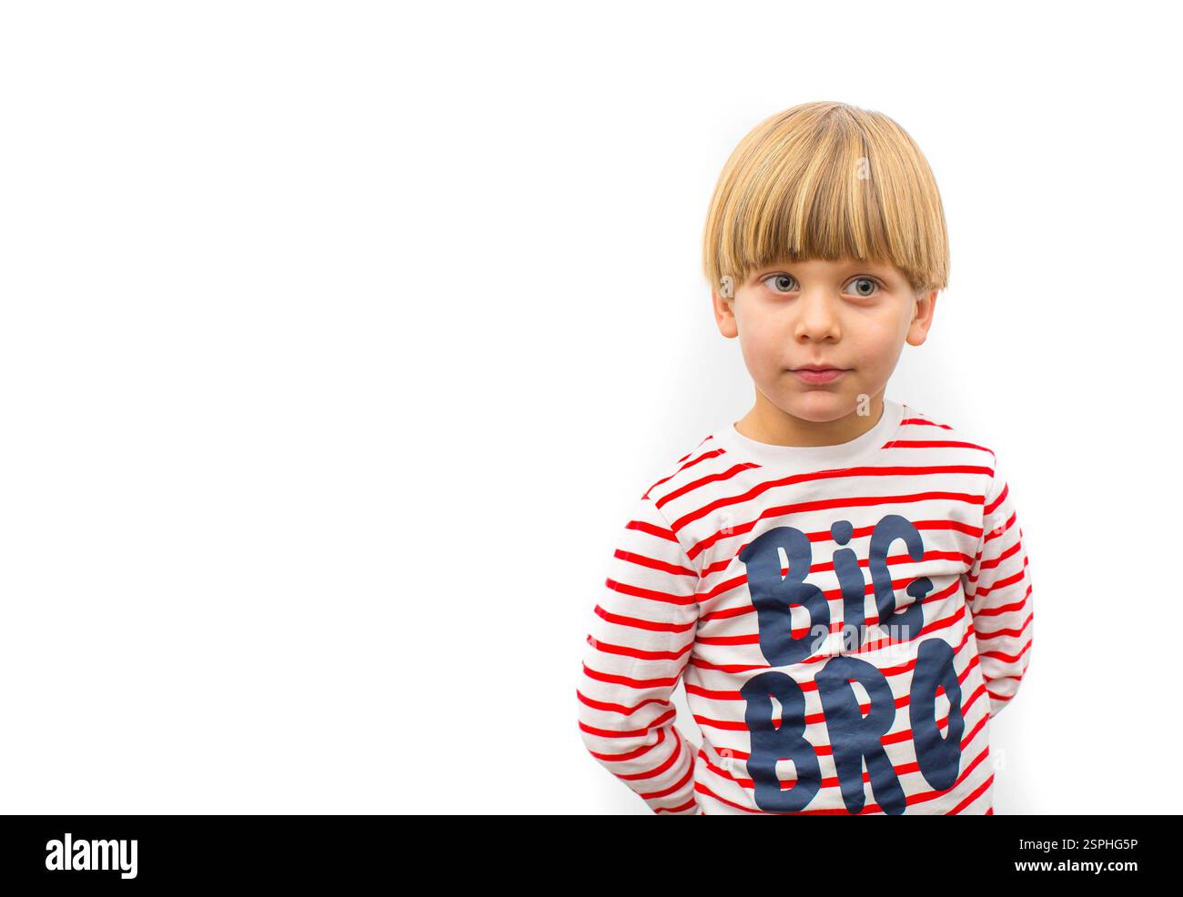 Un ragazzo allegro indossa con sicurezza una camicia a righe rosse con lettere stampate, fotografata su uno sfondo bianco brillante, che trasuda un se Foto Stock