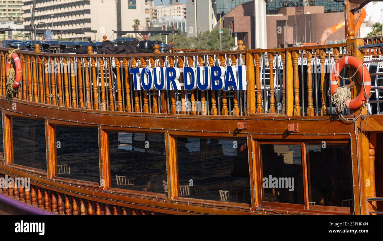 Dubai, Emirati Arabi Uniti - 13 novembre 2024: Dhow tradizionale in legno con cartello "Tour Dubai" nel Dubai Creek, Emirati Arabi Uniti. Tour in barca che mostra il patrimonio, il turismo e il paesaggio urbano Foto Stock
