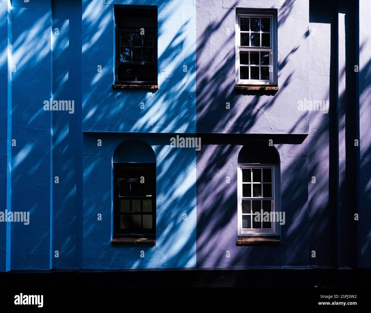 Quattro finestre sulla facciata della casa blu e viola con sole parziale e ombre inclinate Foto Stock