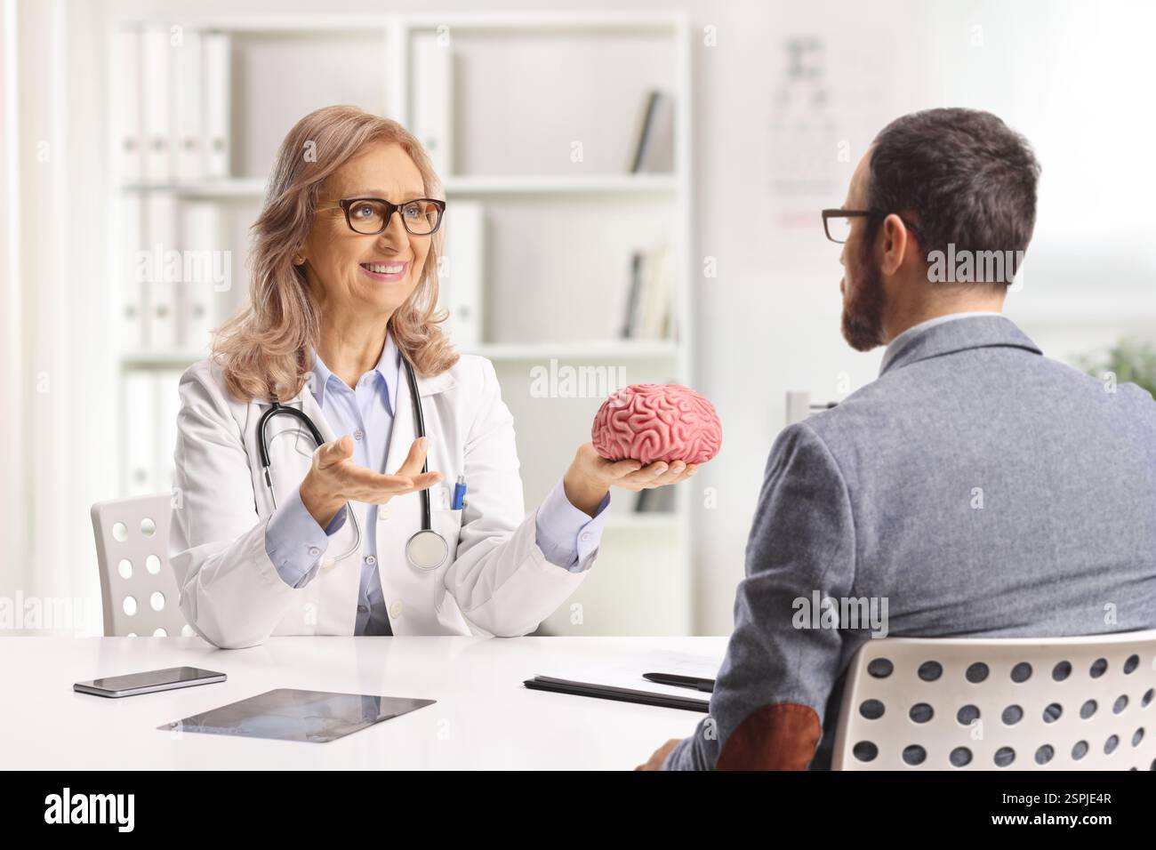 Neurochirurgica femminile seduta con un paziente e con un modello cerebrale in ufficio Foto Stock