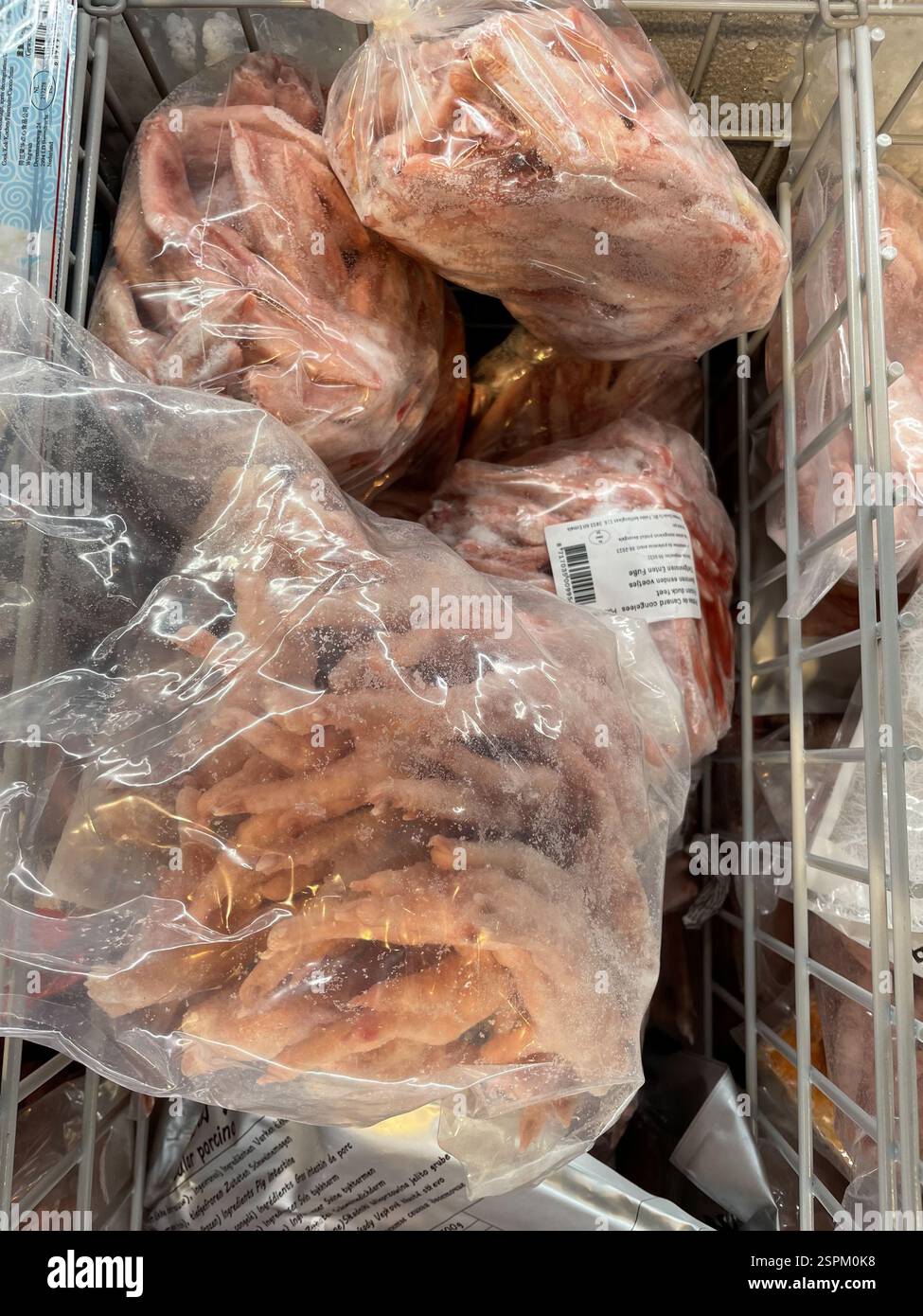 Più sacchetti di piedini di pollo congelati sono impilati in una vetrina del congelatore. I piedi sono rosa chiaro e i sacchetti sono di plastica trasparente, che mostra il profarmaco Foto Stock