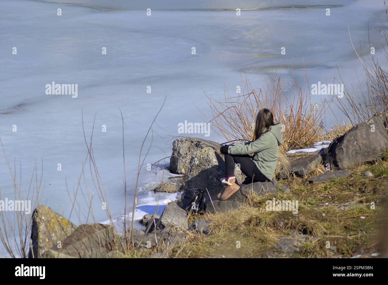 Giovane donna seduta sulla riva del fiume che guarda lontano dal fiume Foto Stock