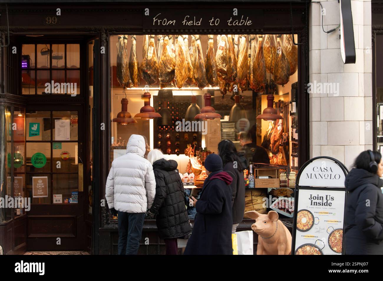 I clienti possono ammirare il prosciutto stagionato appeso alla finestra di Casa Manolo, un ristorante spagnolo di tapas al 99 Strand, Londra. Stanno pensando di cenare all'interno. Foto Stock