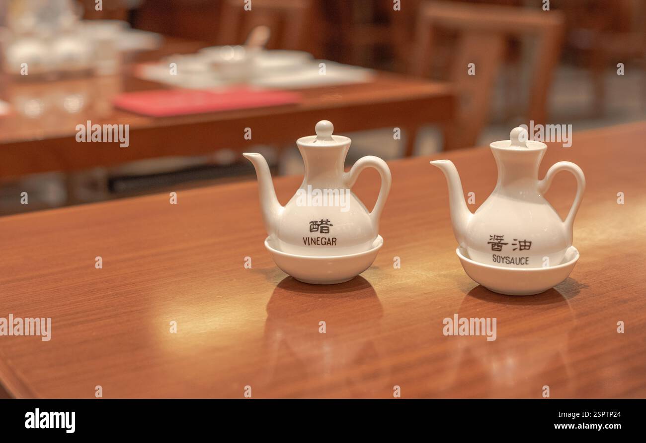 Aceto e salsa di soia in caraffe di ceramica, in ciotole, in cima a un tavolo di legno in un ristorante. Foto Stock