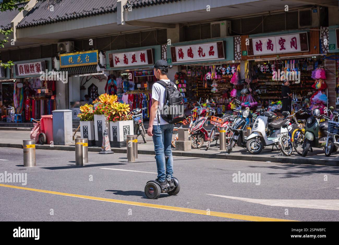 Shanghai, Cina - 27 settembre 2018: Un giovane uomo cinese cavalca uno skateboard su strada, passando davanti a una fila di moto e scooter. Foto Stock Shanghai, Cina - 27 settembre 2018: Un giovane uomo cinese cavalca uno skateboard su strada, passando davanti a una fila di moto e scooter. Foto Stock