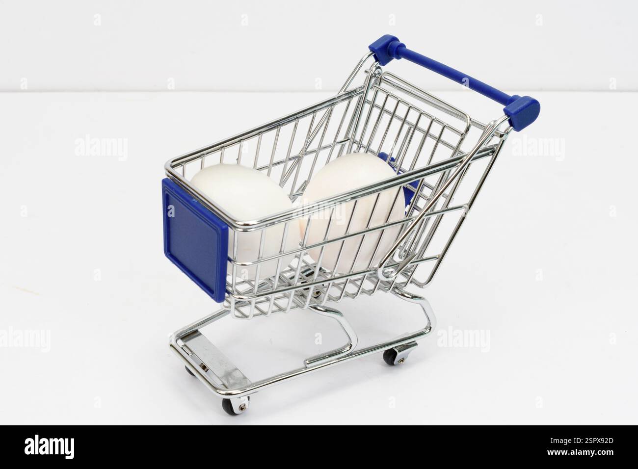 Colpo orizzontale di un piccolo carrello della spesa che regge due uova bianche su bianco. Foto Stock