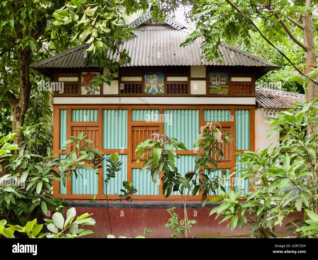 Tradizionale fattoria di campagna del Bangladesh che presenta un'architettura vernacolare con pareti in stagno ondulato, cornici in legno e vegetazione lussureggiante. Foto Stock