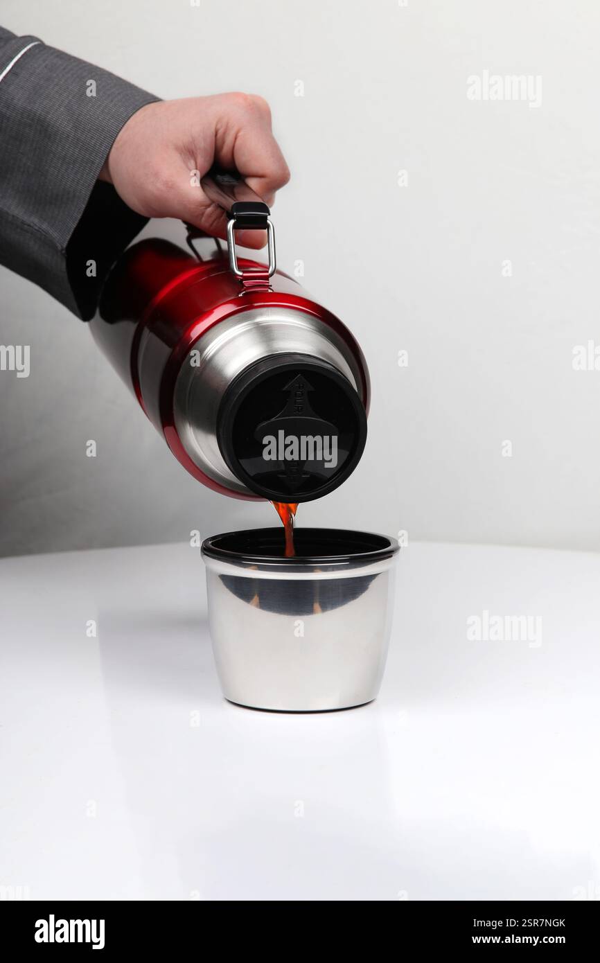 Versare caffè caldo da una termocamera rossa in acciaio inossidabile in una tazza di metallo – concetto di viaggio, campeggio e bevande all'aperto Foto Stock