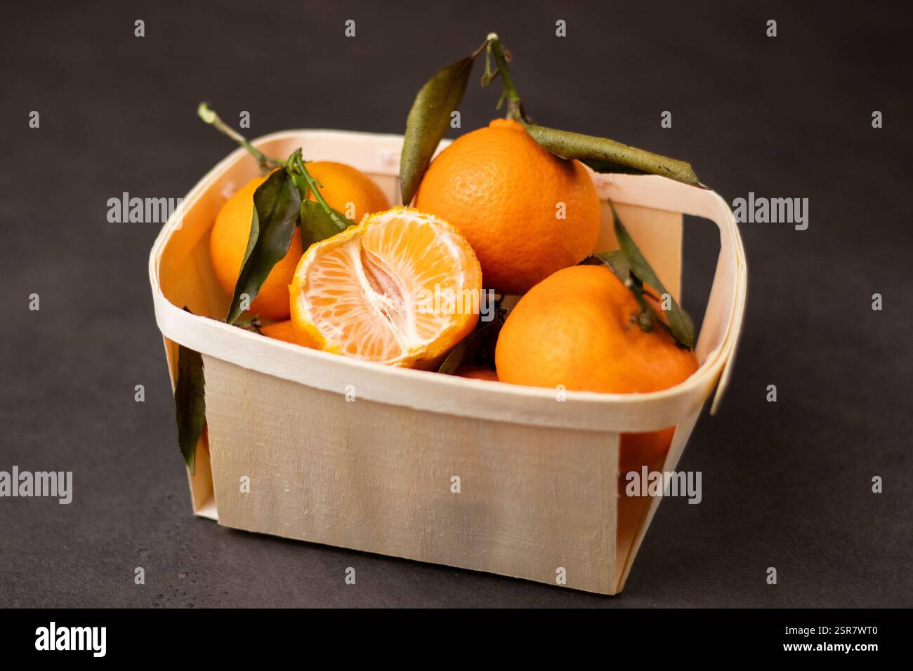 Primo piano di mandarini interi e un frutto pelato in una scatola di legno su sfondo grigio Foto Stock