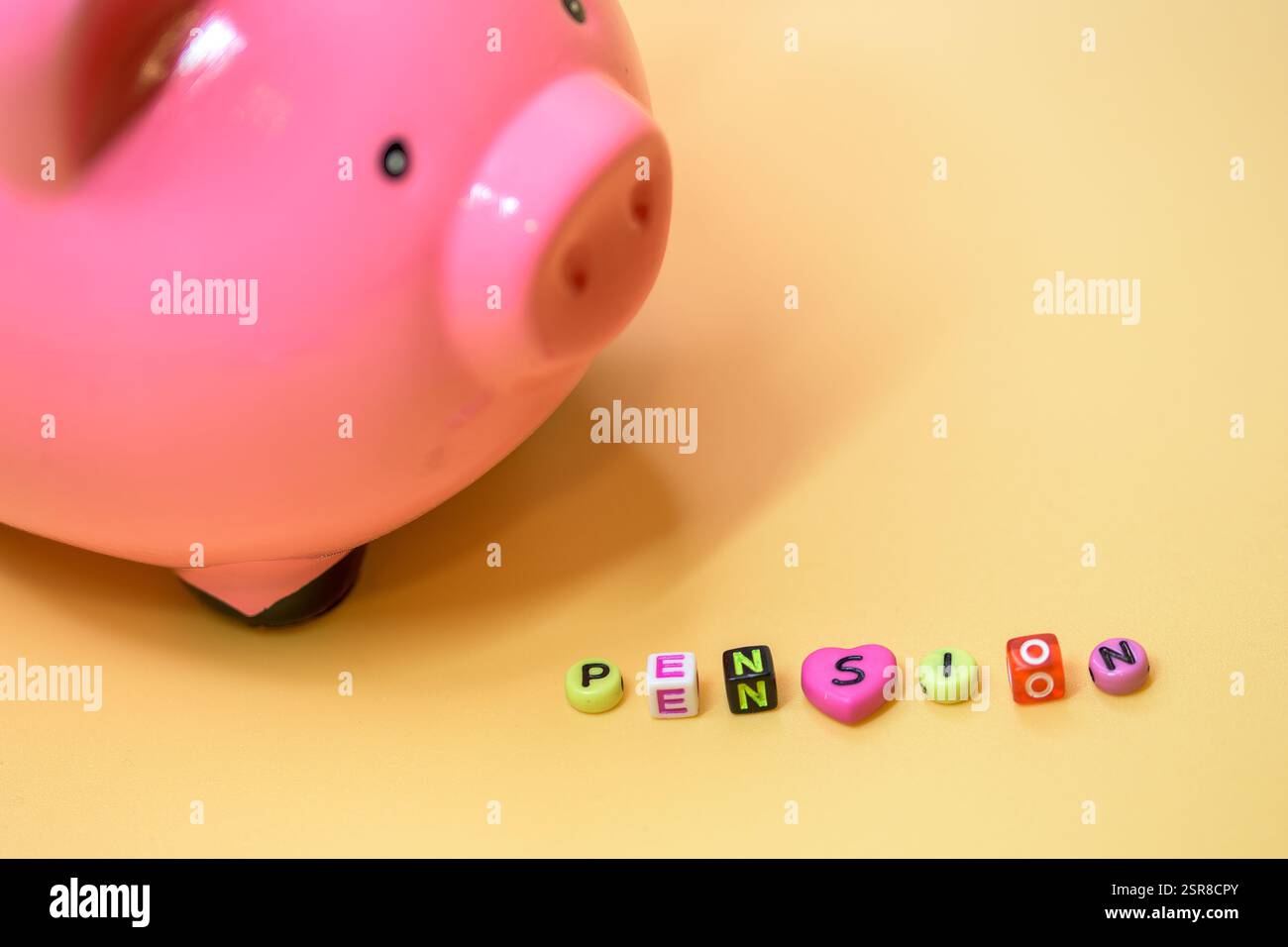 Un salvadanaio rosa accanto alle perline che scrivono "Pension", che rappresenta risparmi e piani finanziari per la pensione, su uno sfondo giallo vibrante Foto Stock