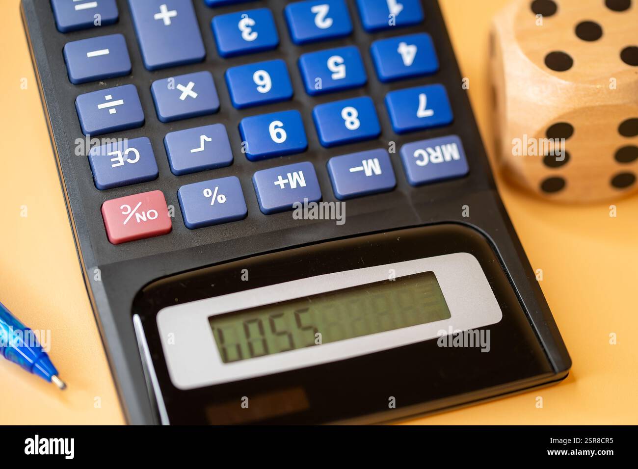 Calcolatrice con display digitale accanto a un dado di legno, che simboleggia il processo decisionale finanziario e la casualità, la perdita Foto Stock