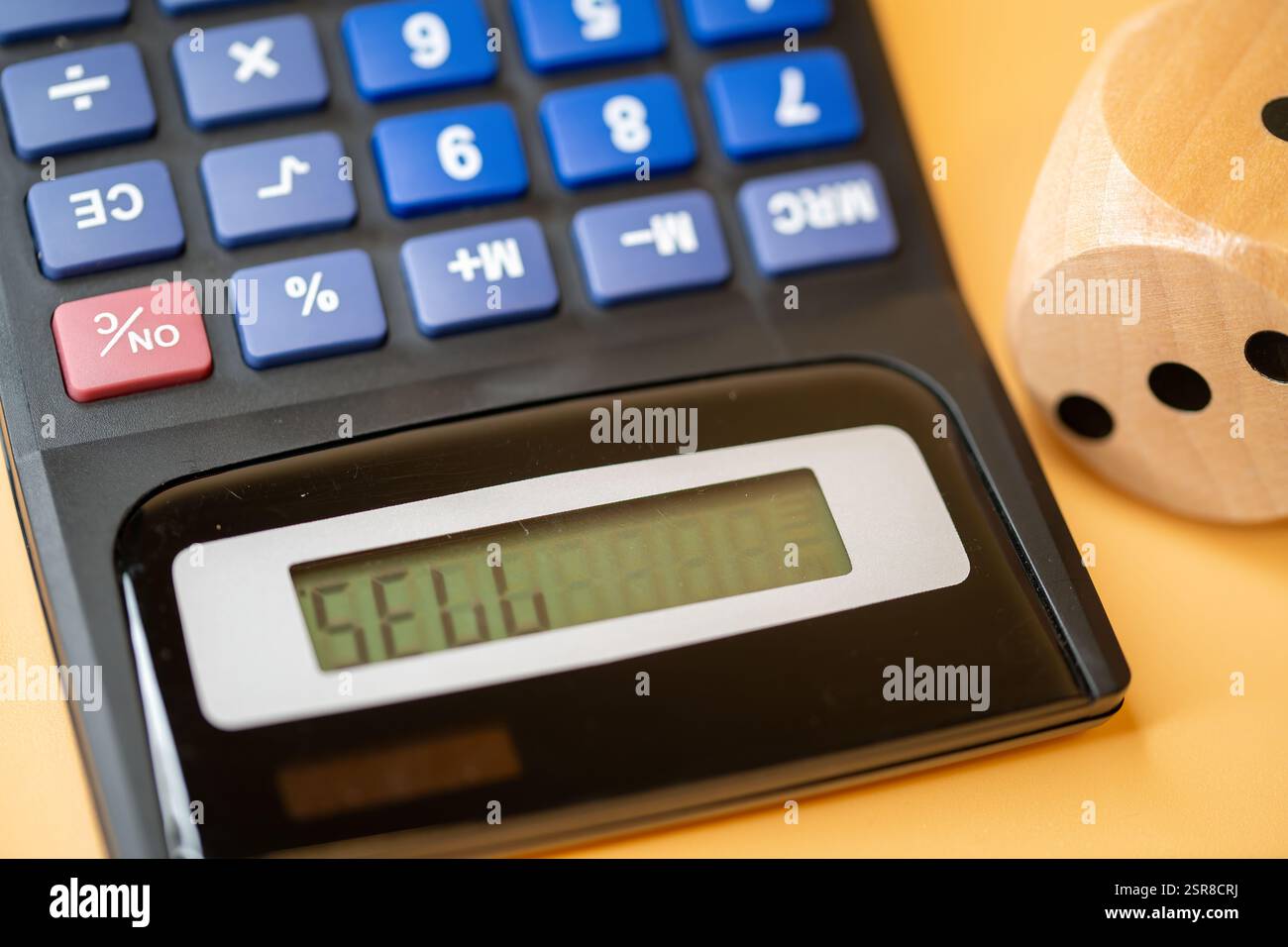 Calcolatrice con un display digitale accanto a un dado di legno, che simboleggia il processo decisionale finanziario e la casualità, vendere, acquistare, Foto Stock