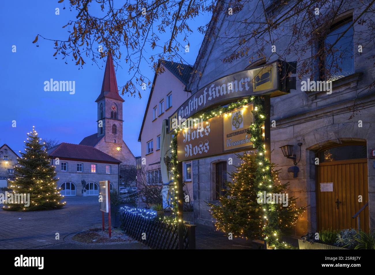 Natale, locanda illuminata al crepuscolo, Chiesa di San Bartolomeo sullo sfondo e albero di Natale illuminato, Eschenau, Franconia media, Baviera, Ger Foto Stock