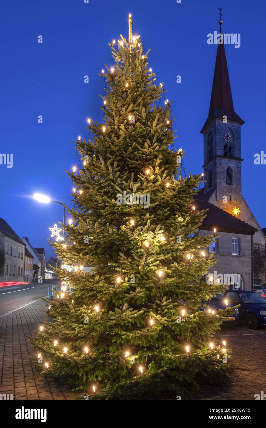 Albero di Natale illuminato sulla piazza del paese al crepuscolo, Chiesa di San Bartolomeo sullo sfondo, Eschenau, Franconia media, Baviera, Germania, EUR Foto Stock